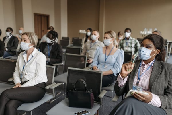 A group of people wearing masks seated in a conference setting, likely attending a business seminar or meeting