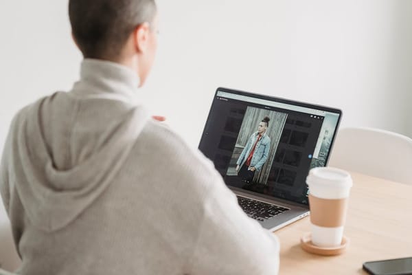 A person in a gray hoodie sits at a wooden table, working on a laptop