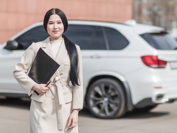 A woman dressed in business attire holding a black folder, standing in front of a white SUV on a sunny day