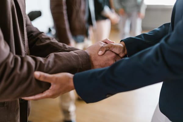 The image shows a close-up of a handshake between two people dressed in business attire, possibly indicating a business meeting or agreement