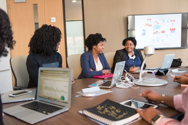 A group of four professionals sitting around a conference table with laptops and notebooks, engaging in a business meeting