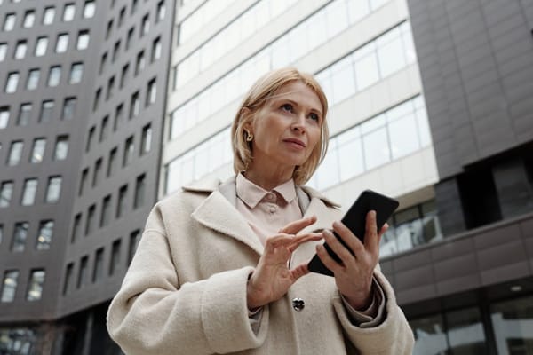 A woman standing outdoors in front of a modern office building, holding a smartphone and looking thoughtful