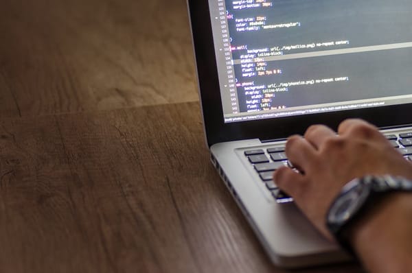 A person is typing on a laptop displaying lines of code