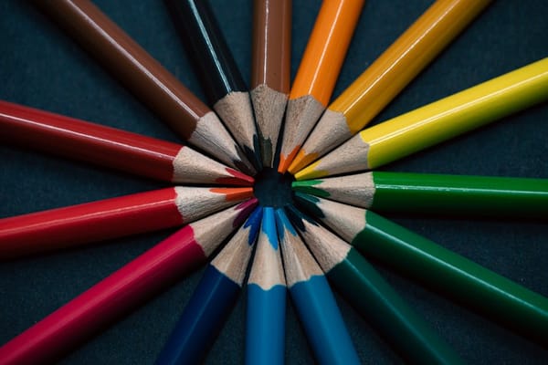 A close-up image of several colored pencils arranged in a circular pattern with their tips pointing towards the center on a dark background