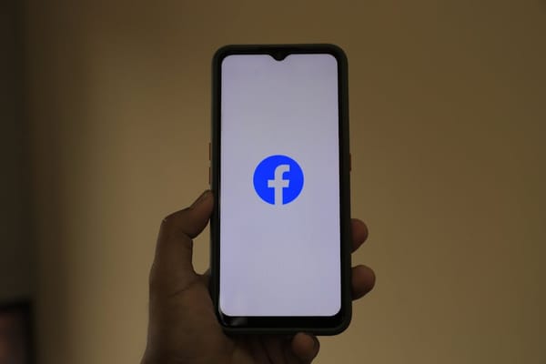 A hand holding a smartphone displaying the Facebook logo on its screen