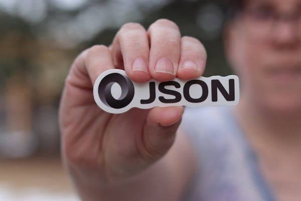 A close-up image of a person's hand holding a sticker with the word 'JSON' on it