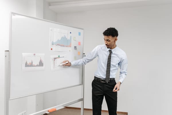 A man in a white shirt and tie presenting data on a whiteboard with charts and graphs