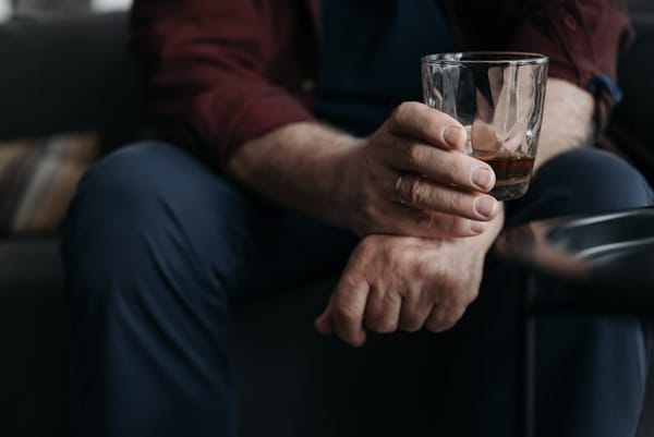 A close-up image of a man seated on a couch, holding a glass of whiskey in one hand