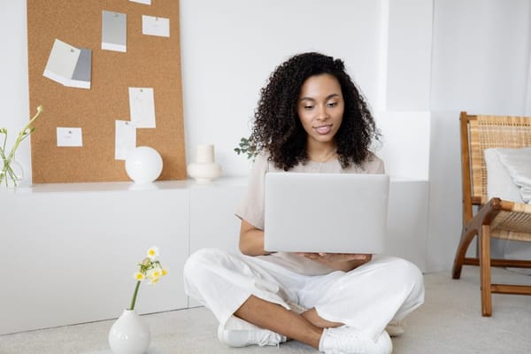 A woman is sitting on the floor with legs crossed, holding and working on a laptop