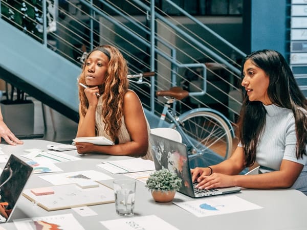 Two women sitting at a desk in an office setting, engaged in a meeting