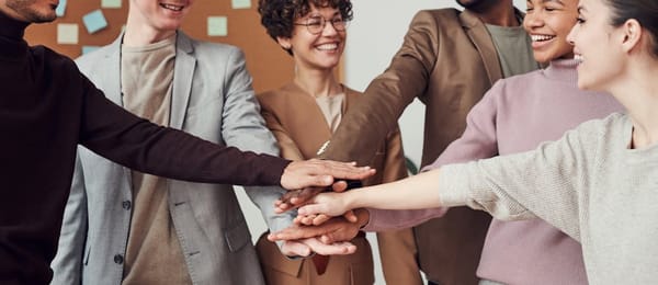 A group of diverse individuals standing in a circle with their hands stacked in the center, symbolizing teamwork and unity in a professional office se