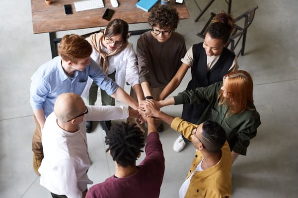 A diverse group of people standing in a circle with their hands placed on top of each other's in the center, symbolizing teamwork and unity