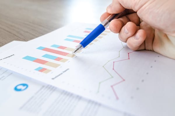 A hand holding a blue pen is pointing at a bar graph on a document