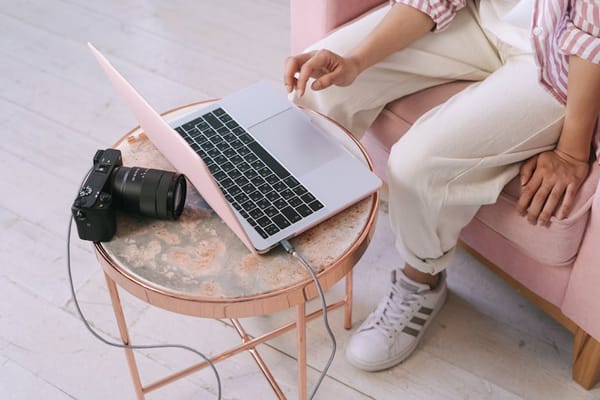 A woman dressed in casual attire sits on a pink chair working on a laptop placed on a round marble table