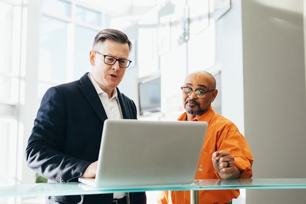 Two men engaged in a discussion while standing in front of a laptop